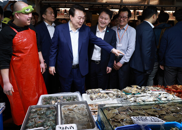 윤석열 대통령이 10일 오후 서울 서대문구 영천시장을 찾아 수산 매장에서 상인과 대화하며 수산물을 살피고 있다. 윤 대통령 오른쪽은 김주현 대통령실 민정수석비서관(연합뉴스)